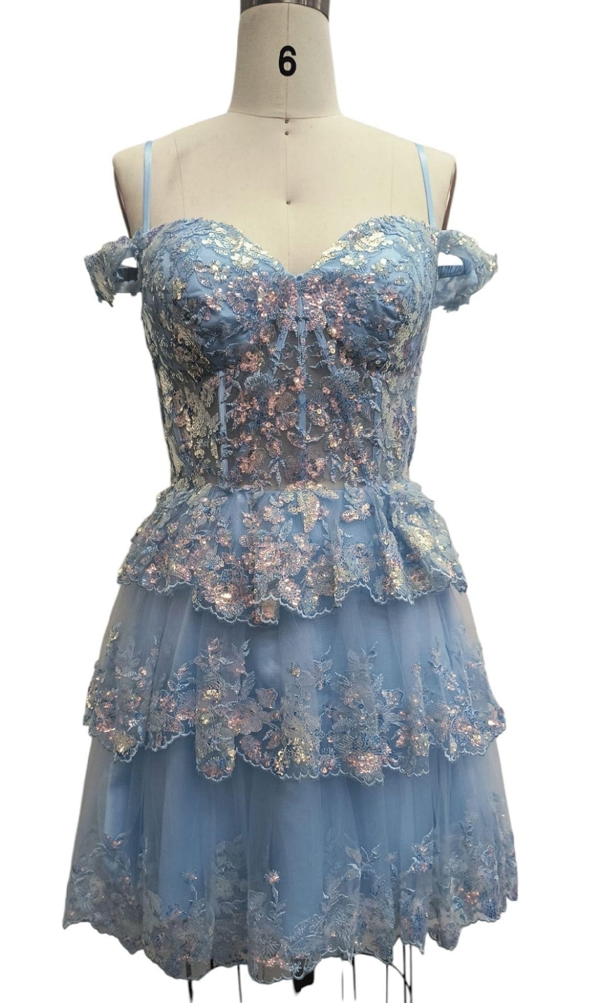 A mannequin showcases the Dave & Johnny 12418 short blue homecoming dress, featuring an off-shoulder layered design, floral embroidery, spaghetti straps, and a flattering corset bodice.